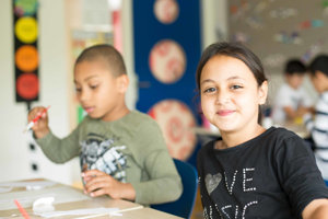 Een jongen en een meisje zijn aan het tekenen in de klas op de basisschool. Het meisje kijkt lachend in de camera. foto: Brenda Roos