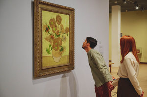 Een jongen kijkt aandachtig naar Van Goghs Zonnebloemen in het Van Gogh Museum. Hij houdt de hand vast van zijn zijn vriendin die achter hem staat. Foto: David Stegenga