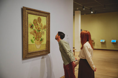 Een jongen kijkt aandachtig naar Van Goghs Zonnebloemen in het Van Gogh Museum. Hij houdt de hand vast van zijn zijn vriendin die achter hem staat. Foto: David Stegenga